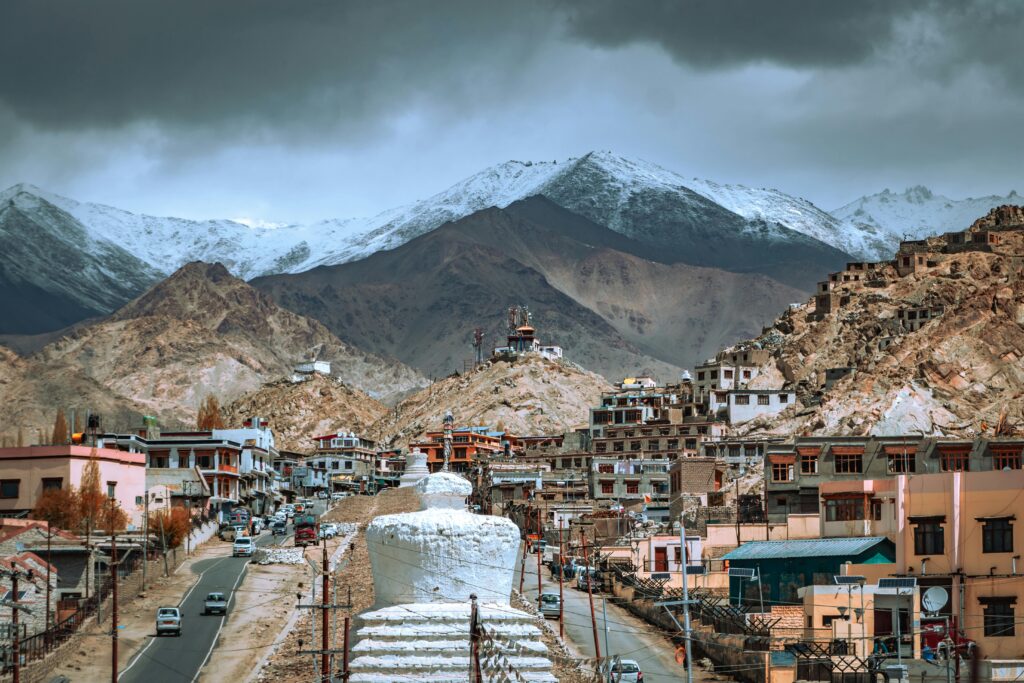 Panoramic view of Leh town with Himalayan mountains and traditional architecture under a dramatic sky.