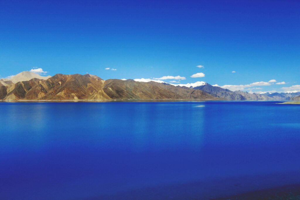 Idyllic view of Pangong Lake with mountains under a clear blue sky, showcasing nature's tranquility.